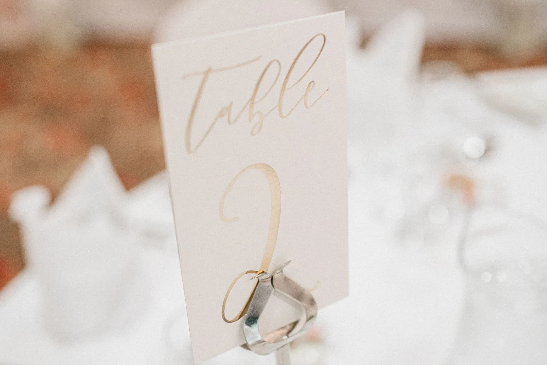 Tarjeta clara con el número de mesa 2 en un soporte metálico sobre una mesa de boda preparada